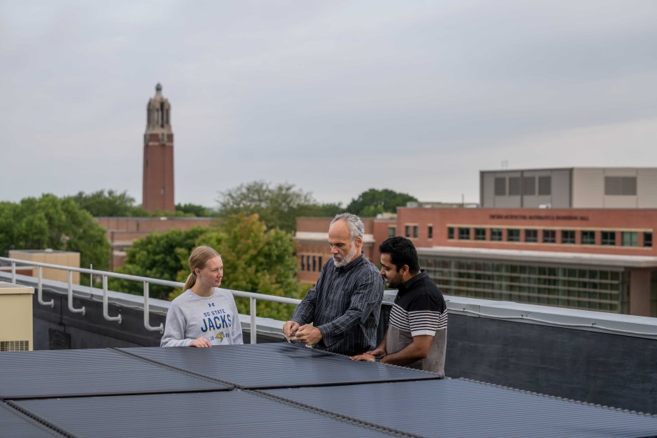 Students and professor on roof with solar panels 