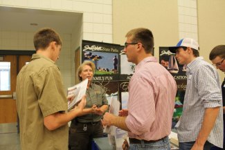 Three male students standing and talking to a lady at a career fair table.