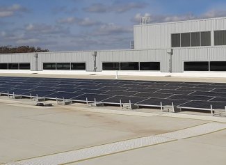 Rows of solar panels on the roof of the SDSU Raven Precision Agriculture building, a gray building stands behind them.